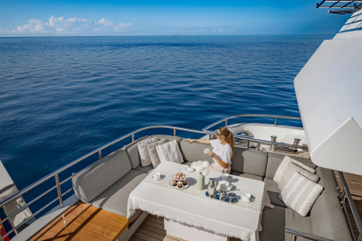 A woman enjoys a beverage on a yacht's deck with a vast blue ocean stretching to the horizon.