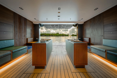 Luxurious wooden interior with plush seating and modern counters in the foreground opens to a serene waterfront view with lush greenery and a cloudy sky in the background.