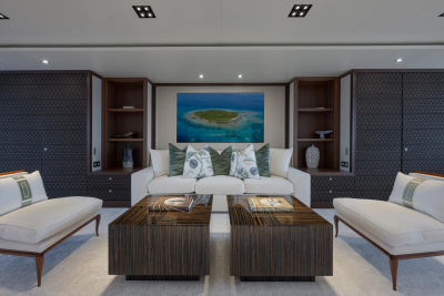 A modern living room with two white sofas and two dark wood coffee tables in the foreground, and a painting of an island in the ocean on the wall in the background.