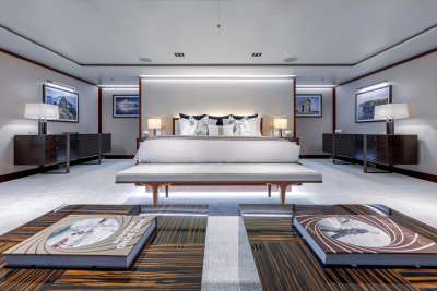 A luxurious bedroom with a large bed and artwork in the background is framed by two wooden tables with books in the foreground.