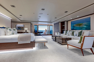 A luxurious bedroom with a large bed in the foreground opens to a balcony with ocean views in the background.
