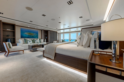 A luxurious yacht master suite with a large bed in the foreground and a seating area with ocean views in the background.