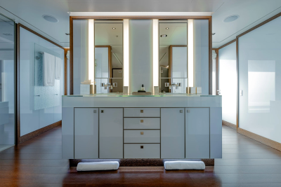 Two neatly folded white towels rest on the dark wooden floor in the foreground, leading to a sleek, modern double vanity with illuminated mirrors in the background.