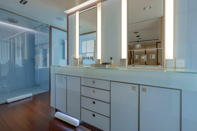 A modern bathroom with a white vanity and glass shower enclosure in the foreground, and reflections of the bathroom in the background mirrors.