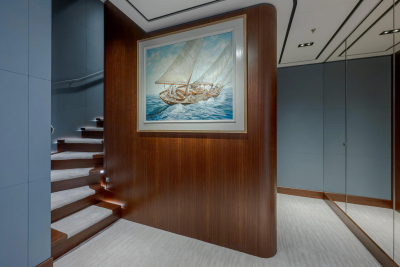 A painting of sailboats hangs on a curved wooden wall next to a carpeted staircase, with a mirrored hallway stretching into the background.