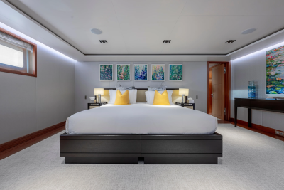 A spacious bedroom with a large bed in the foreground and a hallway with artwork in the background.