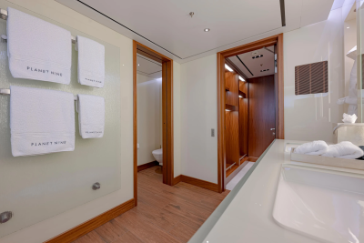 White towels hang on a rack in the foreground of a modern bathroom with a wooden-paneled closet and a glimpse of a toilet in the background.