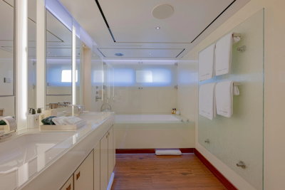 A modern bathroom with a double vanity in the foreground and a bathtub with frosted glass enclosure in the background.
