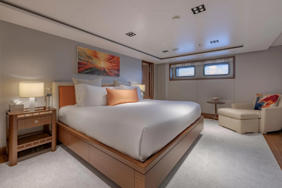 A luxurious bedroom with a large bed in the foreground and porthole windows in the background.