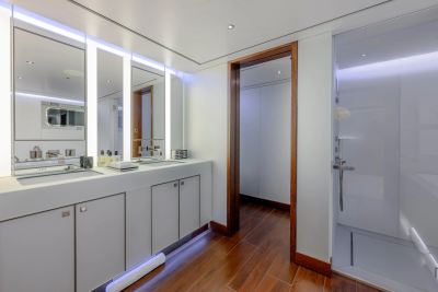 A modern bathroom with a double vanity and mirrors in the foreground, and a doorway leading to a shower stall in the background.