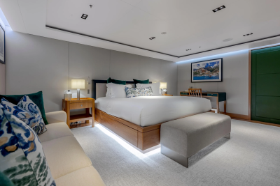 A luxurious bedroom with a large bed and plush seating in the foreground, and a desk with artwork on the wall in the background.