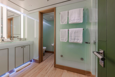 A modern bathroom with a vanity and mirror in the foreground and a doorway leading to a toilet in the background.