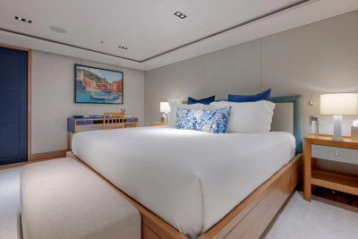 A luxurious bedroom with a large white bed in the foreground and a desk with a painting on the wall in the background.