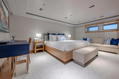 A luxurious bedroom with a large bed and a desk in the foreground, and a sofa and porthole windows in the background.