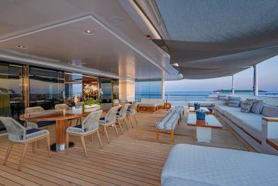 A spacious yacht deck with a dining area in the foreground and a lounge area overlooking the ocean in the background.