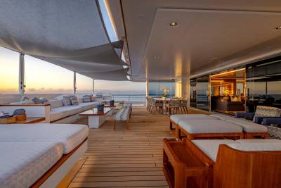 Luxurious lounge seating and a dining area on a yacht's deck overlook a serene ocean sunset.