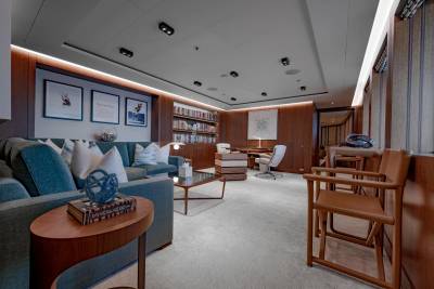 A plush teal sofa with decorative pillows sits in the foreground, while a well-stocked bookshelf and a modern office space fill the background of this luxurious room.