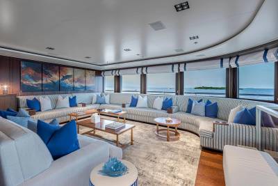 A spacious, modern yacht lounge with plush seating and ocean views is in the background, while a contemporary coffee table arrangement sits in the foreground.