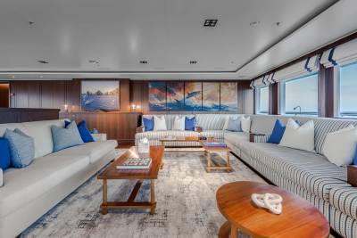Plush sofas and wooden coffee tables fill the foreground of a spacious living area, while a wall of windows and vibrant artwork adorn the background.