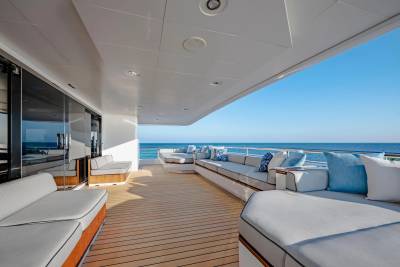 A spacious yacht deck with plush white seating and blue accents overlooks a calm, blue ocean under a clear sky.