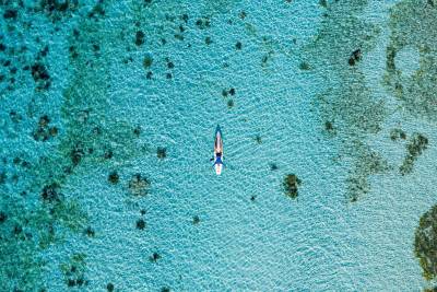 A person lies on a paddleboard in crystal-clear turquoise water, with coral reefs visible beneath the surface.