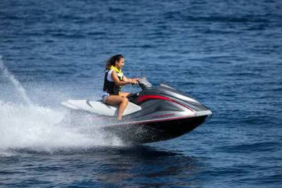 A woman rides a jet ski through the blue ocean, leaving a trail of white spray.