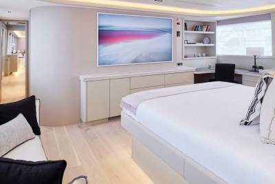 A luxurious bedroom on a yacht features a large bed in the foreground and a hallway visible in the background.