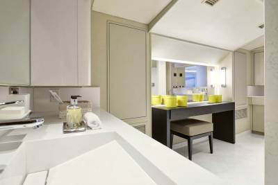 A modern white sink and countertop fill the foreground, while a vanity with yellow containers and a large mirror stretches across the background.