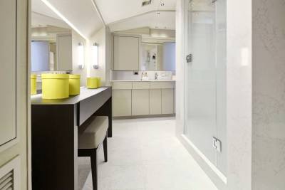 A modern, well-lit bathroom with a vanity and stool in the foreground and a shower stall in the background.