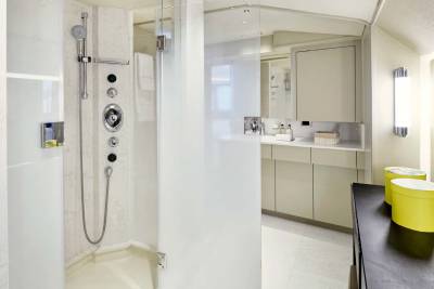 A modern bathroom features a sleek shower stall in the foreground and a vanity area with bright yellow containers in the background.