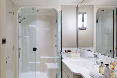 A modern yacht bathroom features a glass-enclosed shower in the foreground and a vanity with a large mirror in the background.