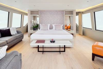A luxurious bedroom with a king-sized bed and plush seating in the foreground is set against a backdrop of large windows offering a bright, airy view.