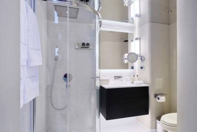 A modern bathroom features a glass-enclosed shower in the foreground and a sleek vanity with a mirror and toilet in the background.