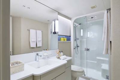 A modern bathroom features a white vanity with a sink and mirror in the foreground, and a glass-enclosed shower with a toilet in the background.