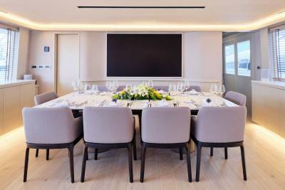 A formal dining table set for a meal is in the foreground, with a large blank screen mounted on the wall in the background.