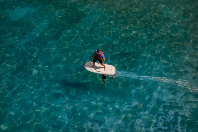 A person on a hydrofoil board glides across the clear, turquoise water, leaving a white wake behind them.