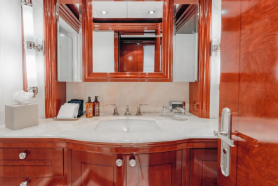 A modern bathroom vanity with a white sink and polished wood cabinetry is in the foreground, while a mirrored cabinet and wall sconces are visible in the background.