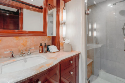 A luxurious bathroom features a marble vanity with a sink in the foreground and a glass-enclosed shower in the background.