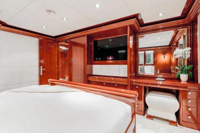 A luxurious bedroom with a large bed in the foreground and a vanity with a mirror and a television in the background.