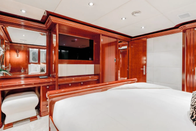 A luxurious bedroom with a plush white bed in the foreground and polished wood cabinetry and a television in the background.