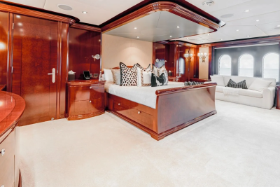 A luxurious bedroom with a large bed and plush carpet in the foreground, and a seating area with a sofa and arched windows in the background.