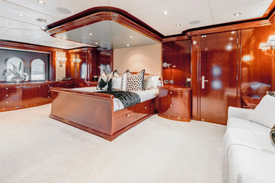A luxurious bedroom with a large bed in the foreground and rich wooden cabinetry and a sofa in the background.
