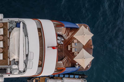 A luxurious yacht with white lounge chairs in the foreground is anchored in the deep blue sea.