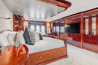 A luxurious yacht bedroom features a plush bed with decorative pillows in the foreground and elegant wooden cabinetry with a television in the background.