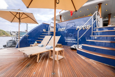 Two lounge chairs and a small table sit on a wooden deck in the foreground, while a large blue yacht with the name "DIRT POOP" is docked in the background.