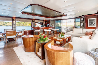 Luxurious yacht interior with plush seating and a bar in the foreground, overlooking a serene body of water and lush green hills in the background.