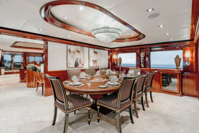 A formal dining room with a large wooden table set for a meal in the foreground, and a view of the ocean through windows in the background.