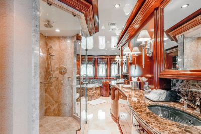 A luxurious bathroom with a marble shower and bathtub in the foreground and a vanity with a large mirror in the background.