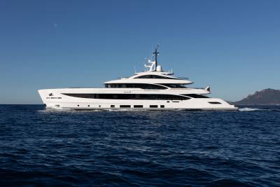 A large white yacht cruises on a deep blue sea under a clear sky with a distant, hazy island.
