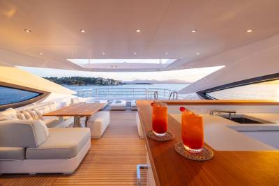 Two tropical cocktails sit on a wooden bar in the foreground, with a luxurious yacht deck and a scenic ocean view in the background.